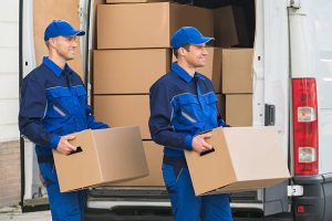 Smiling young delivery men carrying cardboard boxes while walking outside truck